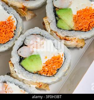 Un piatto bianco è riempito con una varietà di involtini di sushi, ricoperti da una deliziosa salsa. Foto Stock