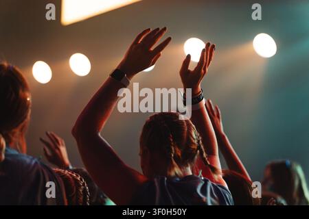 Persone che alzano le mani in adorazione o durante un concerto con illuminazione scenica Foto Stock
