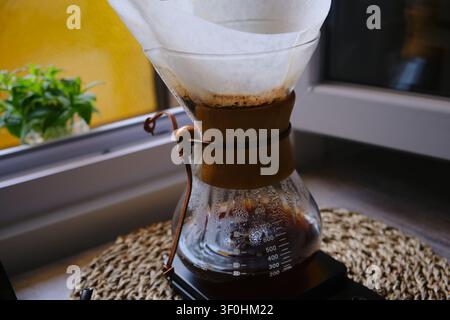 Versare acqua calda sui fondi di caffè in una caffettiera in vetro Chemex Foto Stock