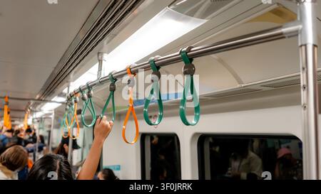 Primo piano delle maniglie sospese all'interno di un treno della metropolitana di Kaohsiung, a Taiwan, con passeggeri in piedi che si aggrappano alle maniglie durante un viaggio urbano. Foto Stock