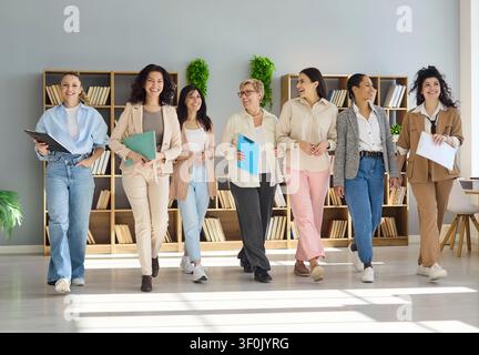 Squadra diversificata di donne d'affari sicure di sé che camminano insieme in un ufficio luminoso sorridendo Foto Stock