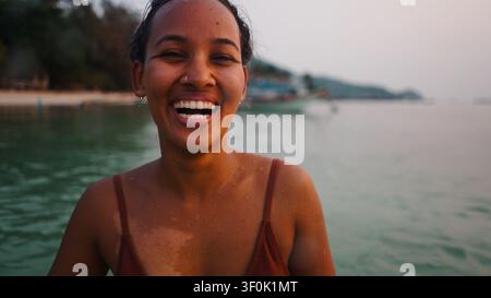 Giovane donna che si gode una vacanza tropicale in spiaggia, ride felicemente nell'acqua dell'oceano Foto Stock