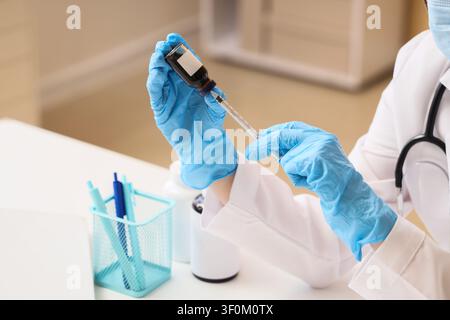 Professionale medico con guanti blu che prepara una siringa con vaccino da una fiala per iniezione, il medico o l’infermiera sta aspirando medicina liquida da una Foto Stock