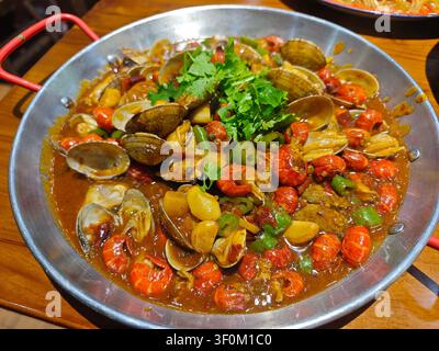 Un piatto di frutti di mare saporito con aragoste e vongole saltate con aglio, peperoncino e coriandolo fresco, servito in una padella di metallo Foto Stock