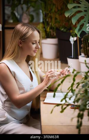 Donna che esamina un siero per la cura della pelle mentre prende appunti di bellezza alla scrivania. Foto Stock