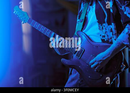 Musicista che suona la chitarra elettrica sotto luci al neon per una campagna musicale Foto Stock
