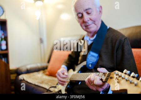 Anziano che si diverte a suonare la sua chitarra elettrica, coltivando un hobby musicale Foto Stock