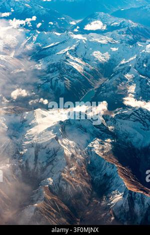 Prospettiva aerea che guarda verso il basso su una vasta catena montuosa coperta di neve con creste affilate e valli glaciali Foto Stock