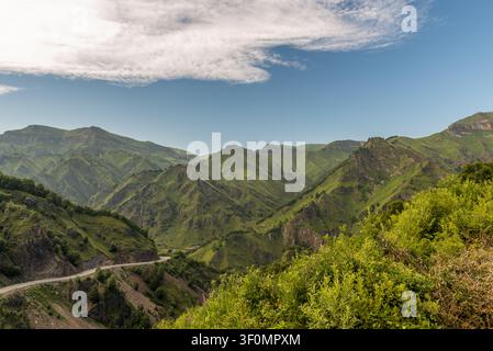 Una vista panoramica ampia di creste montuose verdi stratificate e una strada stretta e tortuosa che attraversa una profonda valle nel Grande Caucaso Foto Stock