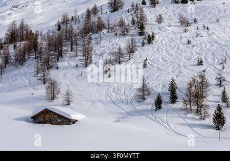 Uno chalet alpino tradizionale in pietra, quasi sepolto sotto una profonda neve invernale, si trova ai piedi di un ampio pendio montuoso nella Valle d'Aosta. Foto Stock