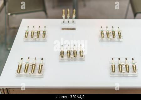Una esposizione di nuove candele di accensione per motori automobilistici disposte su supporti in acrilico trasparente su un tavolo bianco, che mostra pezzi di ricambio per la manutenzione del veicolo Foto Stock