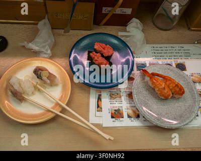 Piatti di nigiri con gamberetti, gunkan al tonno e sushi con bacchette sul bancone di un ristorante sushi con nastro trasportatore a Shibuya, Tokyo, Giappone Foto Stock
