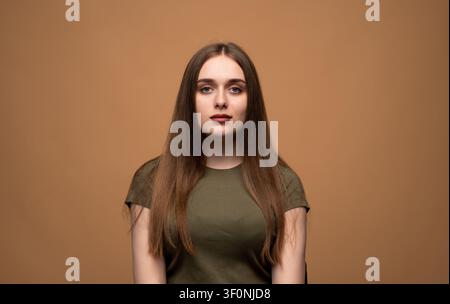 Giovane donna con lunghi capelli castani che posa con sicurezza in un ritratto in studio, incarnando giovinezza, bellezza ed espressione naturale per la pubblicità Foto Stock