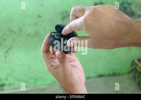 Mani che rimuovono auricolari wireless dalla custodia di ricarica, primo piano con sfondo verde sfocato Foto Stock