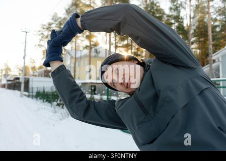 Prima piano di un uomo di mezza età che esegue flessioni laterali con le braccia alzate all'aperto. Si riscalda in una mattina gelida, concentrandosi sui muscoli del tronco. Foto Stock