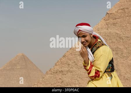 Ritratto autentico di un giovane artista culturale gioioso in un abito folkloristico arabo giallo ornato che aggiusta la fascia turban mentre sorride alla telecamera davanti Foto Stock