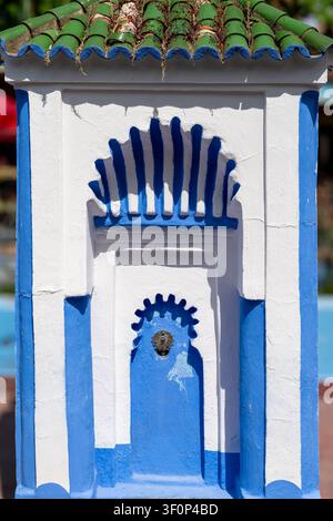 Un primo piano di una piccola fontana ornamentale o di una nicchia murale decorativa nella piazza presenta un arco intagliato a forma di ventaglio con piastrelle geometriche blu e bianche Foto Stock