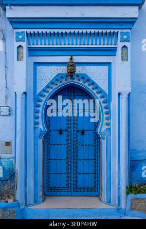 Una porta in legno blu splendidamente ornata presenta un elaborato arco a ferro di cavallo appuntito scolpito con rilievi in stucco, borchie di ferro e un grande battente centrale Foto Stock