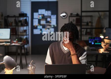 Uomo nero che lavora fino a tardi sul laptop e sente lo stress sul posto di lavoro Foto Stock