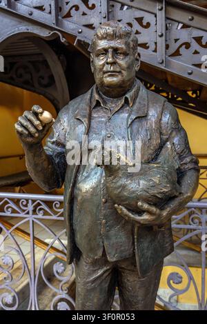 Statua di bronzo di Gyula Krúdy che tiene un pollo e un uovo, all'interno della storica Hall del Mercato Centrale di Budapest, Ungheria Foto Stock