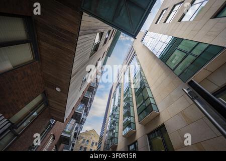Guarda verso l'alto tra edifici moderni con finestre di vetro che riflettono il cielo, Docklands Dublino, Irlanda Foto Stock