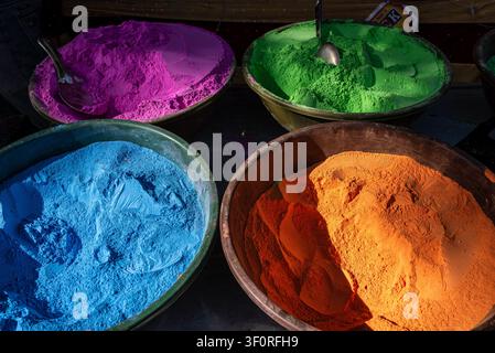 Quattro grandi ciotole di plastica contengono mucchi di polvere colorata vivace in sfumature di magenta, verde, blu brillante e arancione. All'interno di alcuni contenitori, met Foto Stock