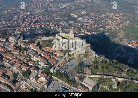Vista aerea della storica fortezza di Guaita Tower sul Monte Titano, circondata da mura in pietra, tetti in terracotta e il paesaggio urbano di San Mari Foto Stock