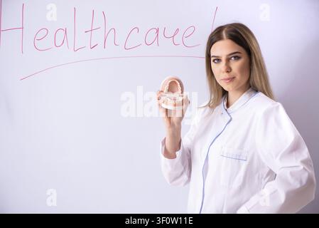 Giovane medico donna in piedi nella parte anteriore del pannello bianco Foto Stock