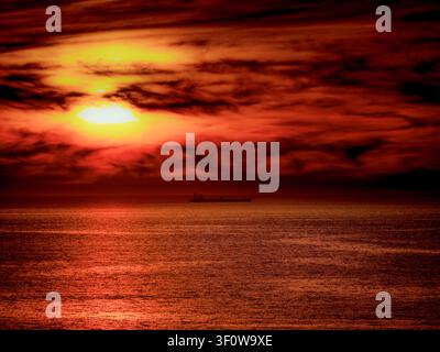 Cielo drammatico e infuocato che regala vivaci tonalità di rosso e arancione con il sole che si fa strada tra le nuvole Foto Stock