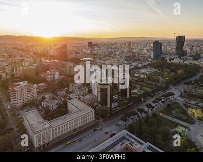 Vista aerea di Tirana al tramonto, con grattacieli moderni, edifici storici e strade urbane, con il caldo bagliore del sole sull'orizzonte i Foto Stock