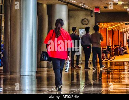 Una donna con un cappotto rosso segue altre persone lungo un corridoio Foto Stock