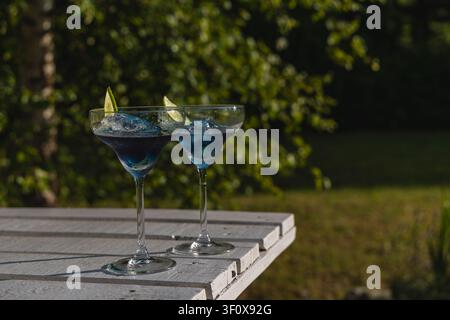 Due cocktail blu in bicchieri con lime sono posati su un tavolo in un giardino sotto la luce del sole. Foto Stock