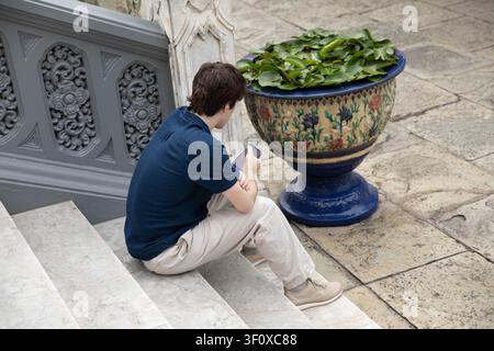 Uomo seduto sulle scale che usa lo smartphone, ripresa ad angolo alto. Foto Stock