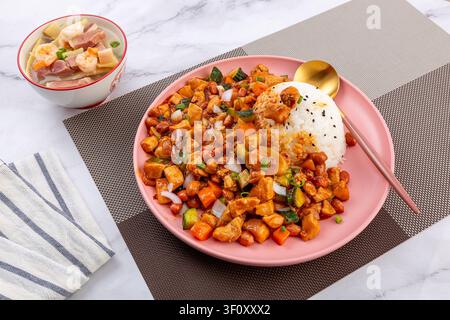 Pollo Kung Pao cinese piccante con arachidi e verdure servito su riso bianco in un piatto rosa. Foto Stock