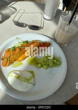 Colazione sana con toast al salmone affumicato, uovo poché, cetriolo fresco e latte servito in un caffè soleggiato. Foto Stock