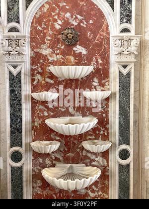 San Pietroburgo, Russia: 8 maggio 2022 - Primo piano di un'elegante fontana da parete classica con ciotole a conchiglia in marmo bianco scolpite montate su rosso venato Foto Stock