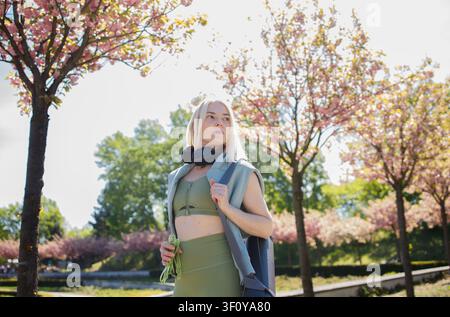 Bella donna bionda di mezza età sportiva con tappetino da yoga e cuffie Foto Stock