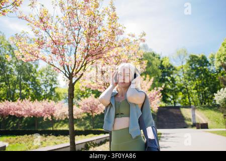 Bellissima donna bionda sportiva con grandi cuffie nella primavera fiorita Foto Stock