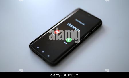 Schermo dello smartphone che mostra una chiamata in arrivo da un chiamante sconosciuto. Foto Stock