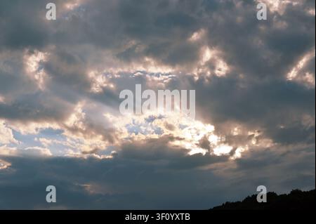 I raggi di sole penetrano attraverso drammatiche nuvole scure creando una scena celeste suggestiva. Foto Stock