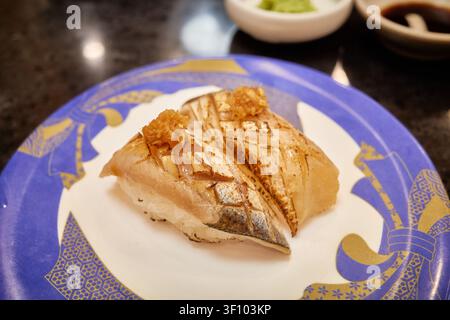 Assortiti di nigiri sushi premium tra cui pesce bianco fresco e pesce scottato con incisioni a croce serviti su piatti colorati a un nastro trasportatore moderno Foto Stock