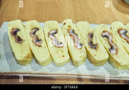 Omelette di uova arrotolata di alta qualità ripiena di anguilla grigliata saporita nota come umaki, servita su un piatto di ceramica che evidenzia l'autentica gastronomia dei frutti di mare asiatici Foto Stock