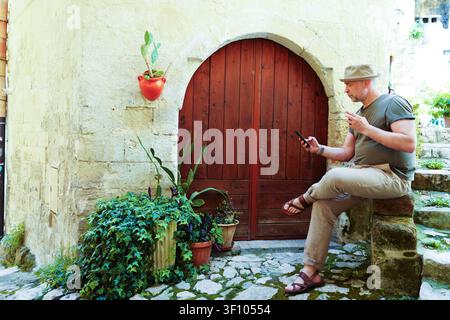 Viaggiatore maturo che riposa sui gradini di pietra in un incantevole cortile mediterraneo con architettura storica e atmosfera di villaggio tradizionale a Matera Foto Stock