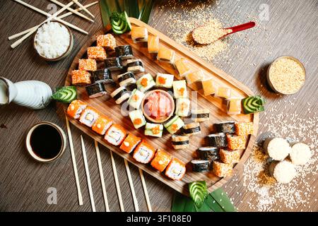 Un vassoio di legno con un assortimento di rotoli di sushi e nigiri, accompagnato da un paio di bacchette. Foto Stock