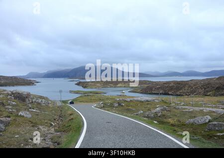 Strada asfaltata deserta che porta verso un fiordo marittimo scenografico e montagne frastagliate nelle Highlands scozzesi, Scozia, Regno Unito Foto Stock