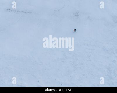 Mikoszewo, Voivodato della Pomerania, Polonia – 20 febbraio 2026: Veduta aerea di due persone che camminano attraverso un vasto paesaggio coperto di neve. Foto Stock