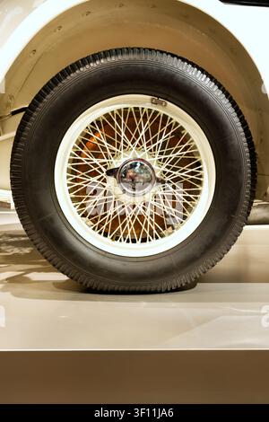Primo piano dettagliato di una ruota di un'automobile classica vintage con raggi in filo bianco, un coprimozzo cromato e un pneumatico retro nero Foto Stock