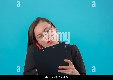 Giovane donna che tiene una clipboard, sembra stanca ed esausta in studio Foto Stock