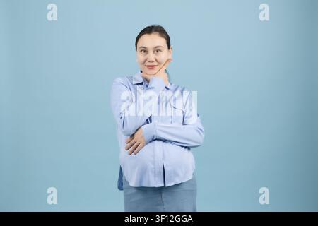 Donna incinta in piedi con le braccia incrociate che sembra sicura di sé in studio Foto Stock