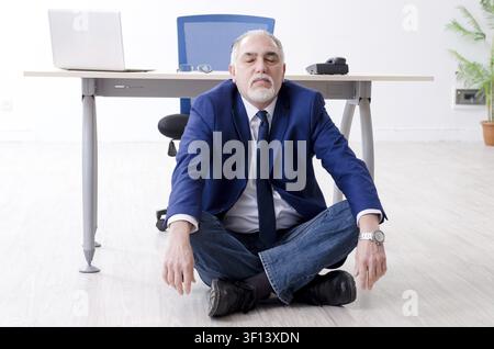 Imprenditore invecchiato facendo esercizi yoga in ufficio Foto Stock